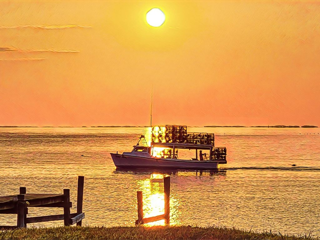 A fishing boat with stacked crab pots sails on calm water at sunset near a wooden dock, showcasing one of the best Labor Day boating destinations.