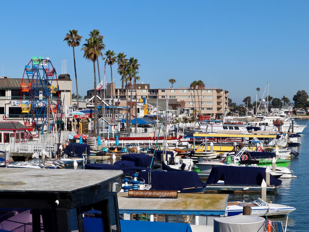 A marina with numerous docked boats, colorful buildings, a Ferris wheel, and Palm Trees.