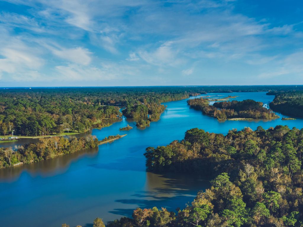 From an aerial view, a winding lake. Vibrant trees form a lush canopy, while calm waters reflect shades of Emerald and Sapphire.