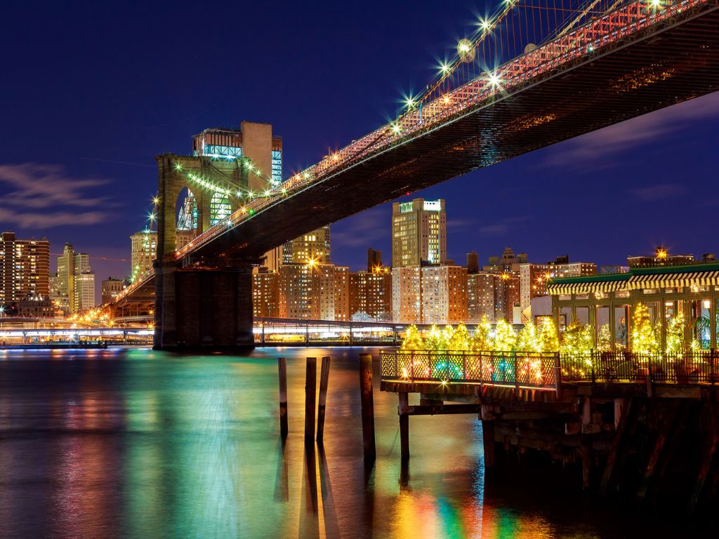 Brooklyn Bridge lit up at night with city buildings and water reflections highlighting its potential as a festive Christmas boating spot.