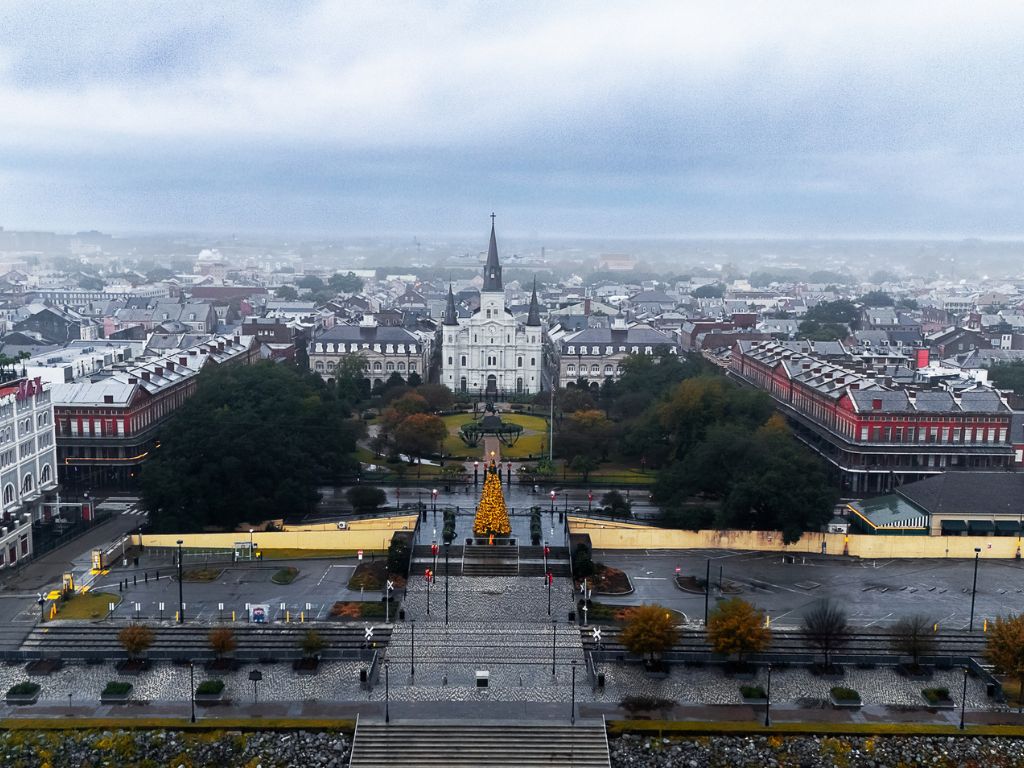 An aerial view of Jackson Square in New Orleans, a charming Christmas boating spot, with St. Louis Cathedral and historic buildings surrounded by trees on a cloudy day.