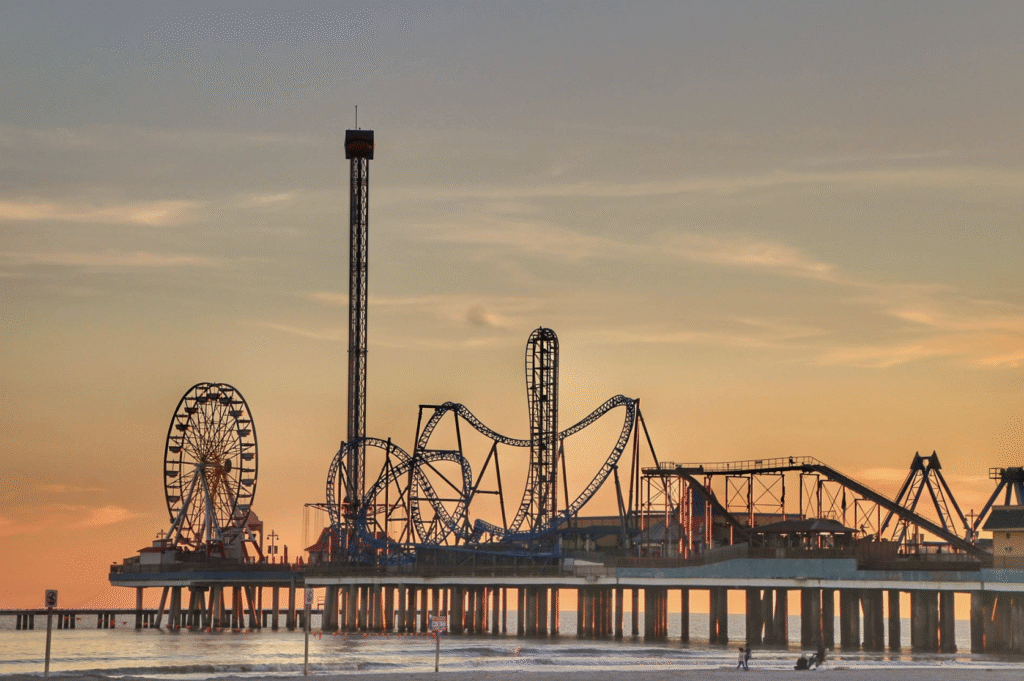 A view of Galveston's theme park at sunset, with a ferris wheel on the left of the image and the beach in the foreground.