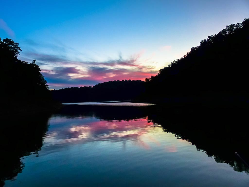 A view across a calm lake in Kentucky just after sunset, with distant clouds reflecting off the water's surface.