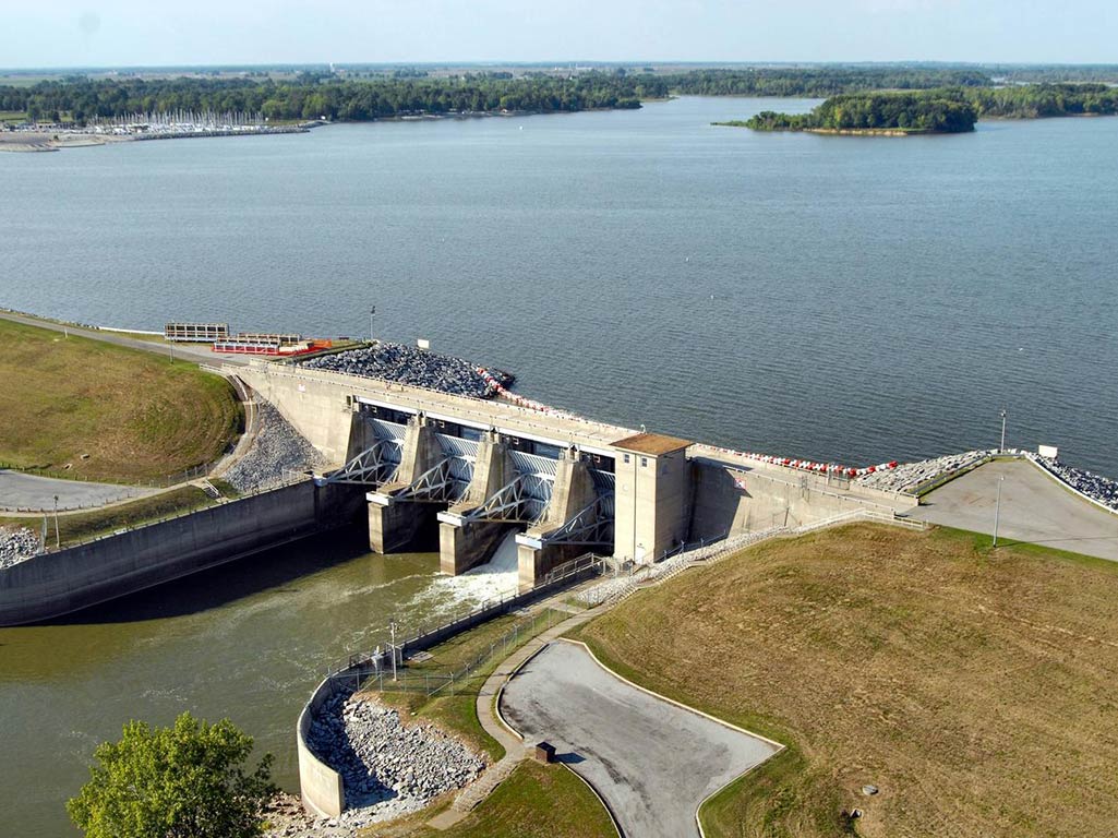 An aerial view of a dam on Carlyle Lake in Illinois, with the calm waters above the dam contrasting with the low-level river beneath on a clear day.