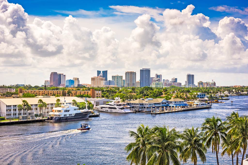 A wide view of Fort Lauderdale's Intracoastal Waterway with yachts, palm trees, and the city skyline under bright skies — a classic winter boating destination.