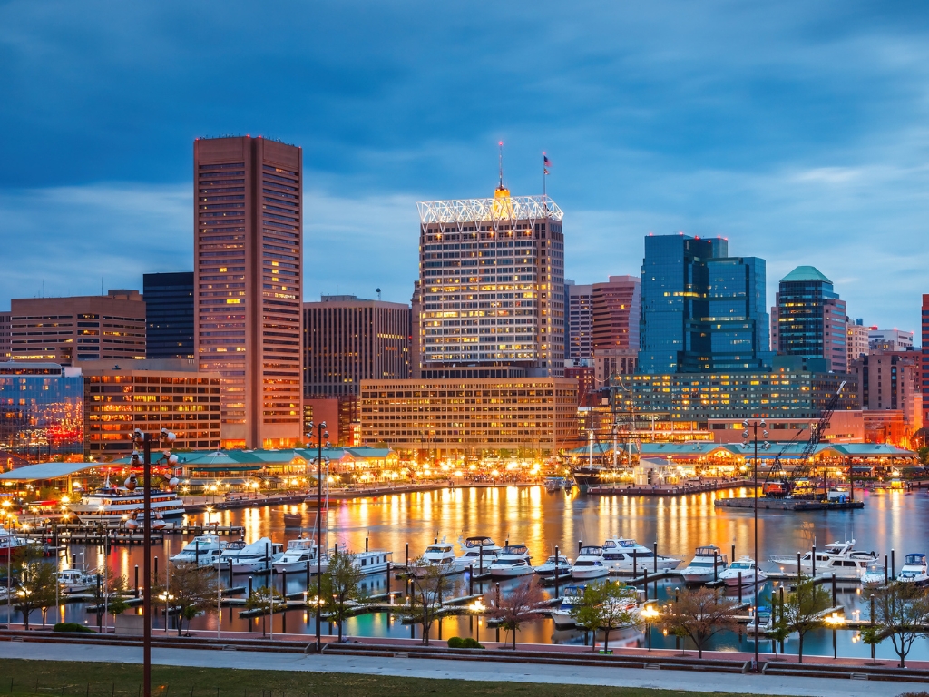 Baltimore Inner Harbor at dusk with city lights reflecting on the water, boats docked along the marina, and the skyline framing a lively winter boating destination.