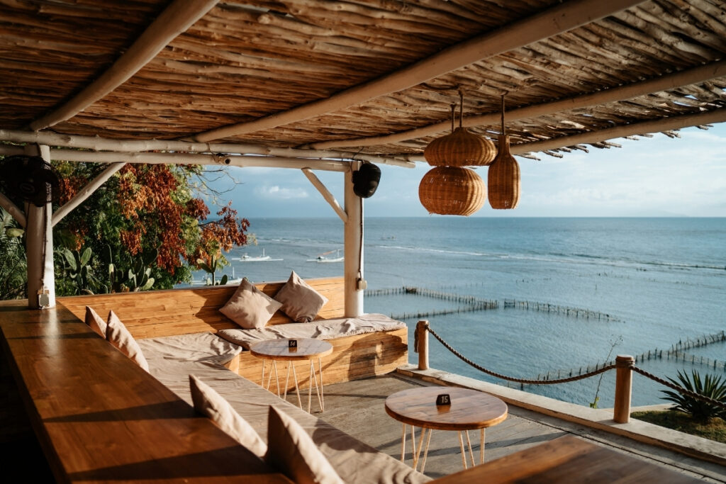 Open-air wooden seating area with tables and cushions overlooks the ocean, featuring hanging wicker lamps and a rustic roof—it's perfect for relaxed boat dining under daylight.