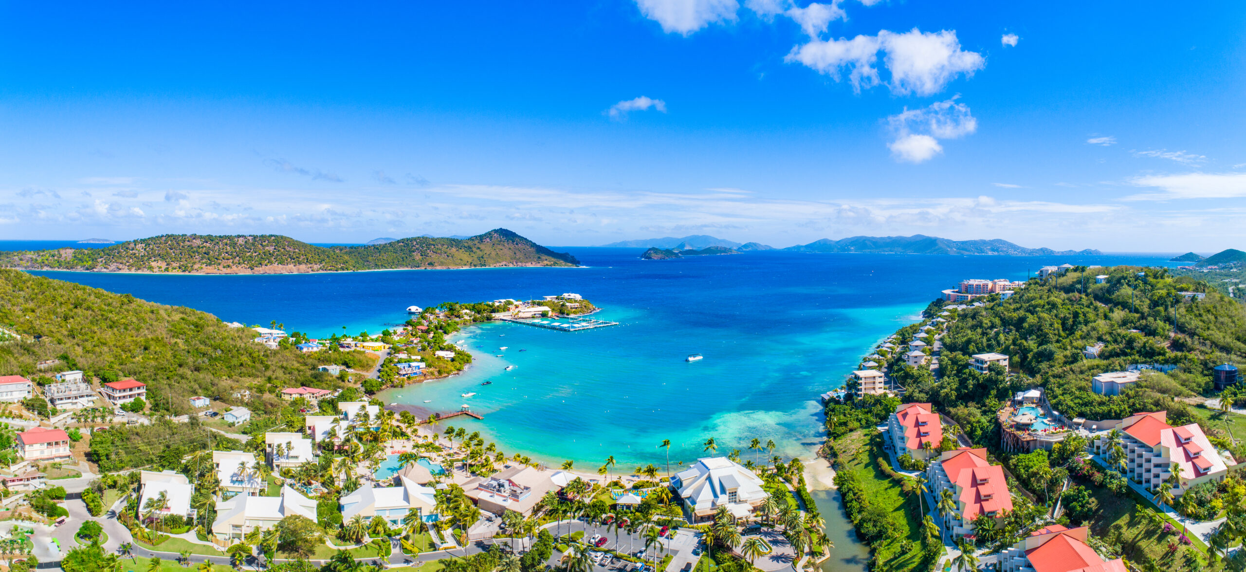 An aerial view of St. Thomas in the US Virgin Islands. The tropical Bay shows turquoise water and beautiful buildings, with lush green vegetation surrounding the shoreline.