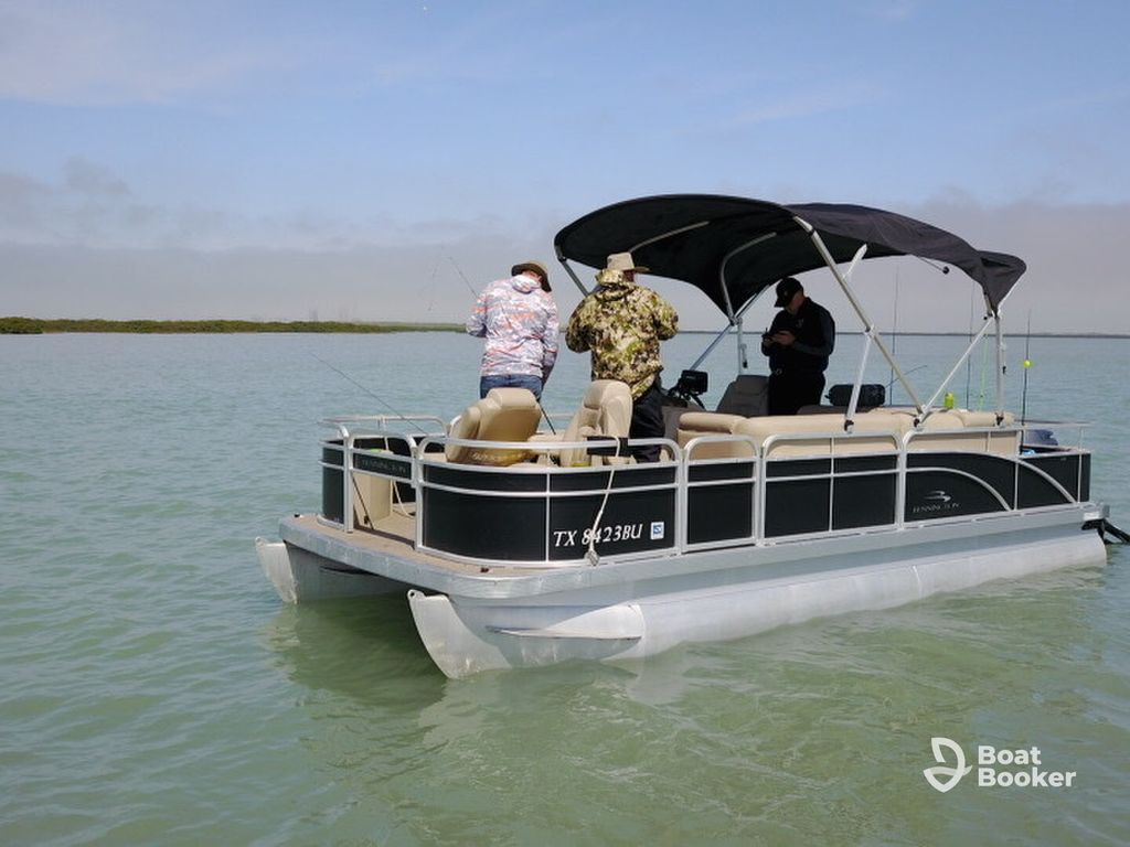 Three people are fishing on a pontoon boat in calm waters with a distant shoreline and clear sky. They're hoping to catch Bass or Trout while enjoying the peaceful scene.