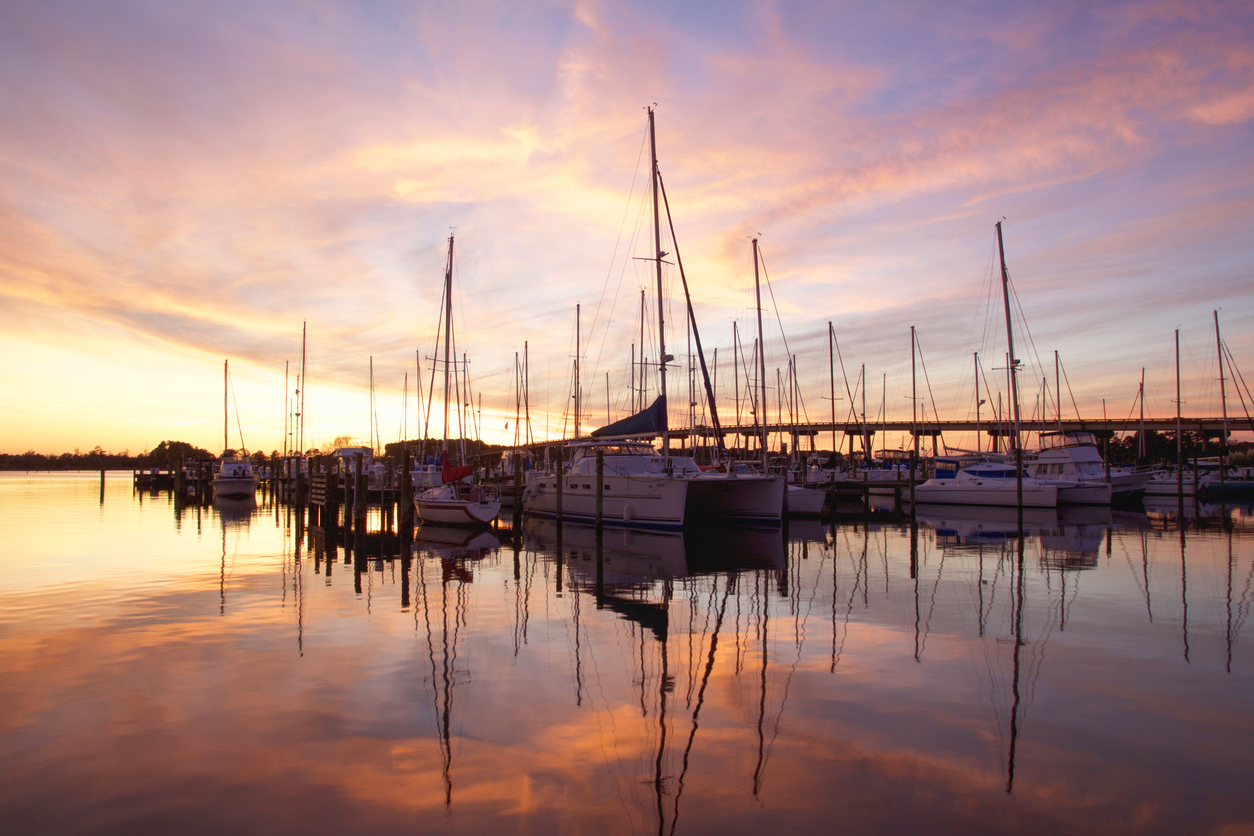 Sailboats docked at a marina with a colorful sunset sky and clouds reflected in the calm water in New Bern, North Carolina