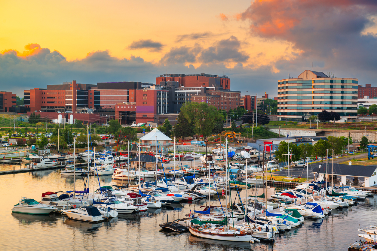 There are lots of docked boats at the marina in the foreground, with modern city buildings behind them at sunset.