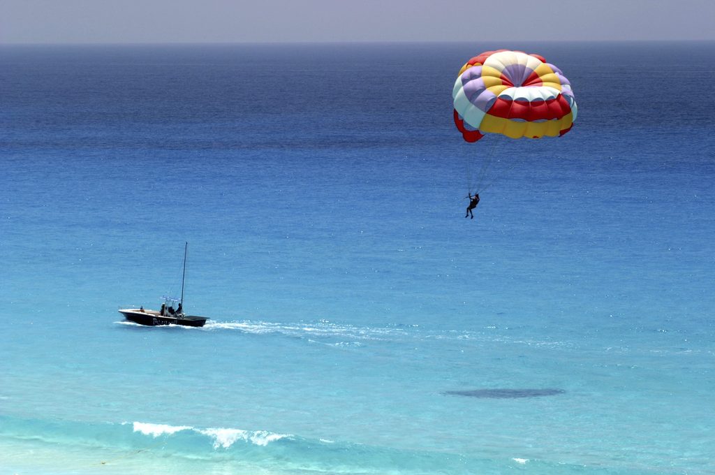 Someone’s parasailing above the ocean, being pulled by a speedboat on clear blue water under a bright sky.