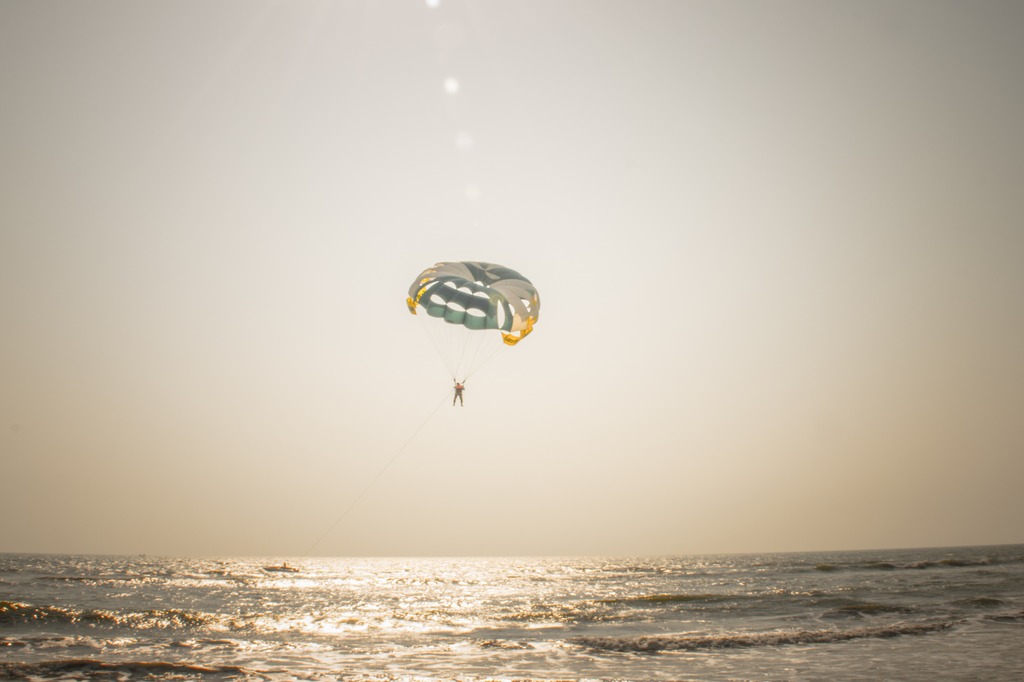 Someone's parasailing over the ocean at sunset, with the parachute open and sunlight shining on the water.