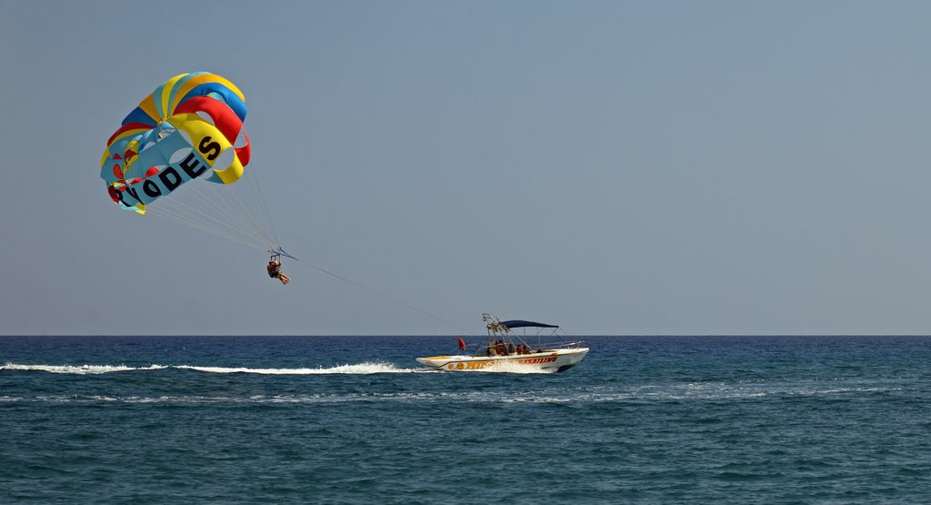 Someone's parasailing with a colorful parachute, being towed by a speedboat over the ocean on a clear day.