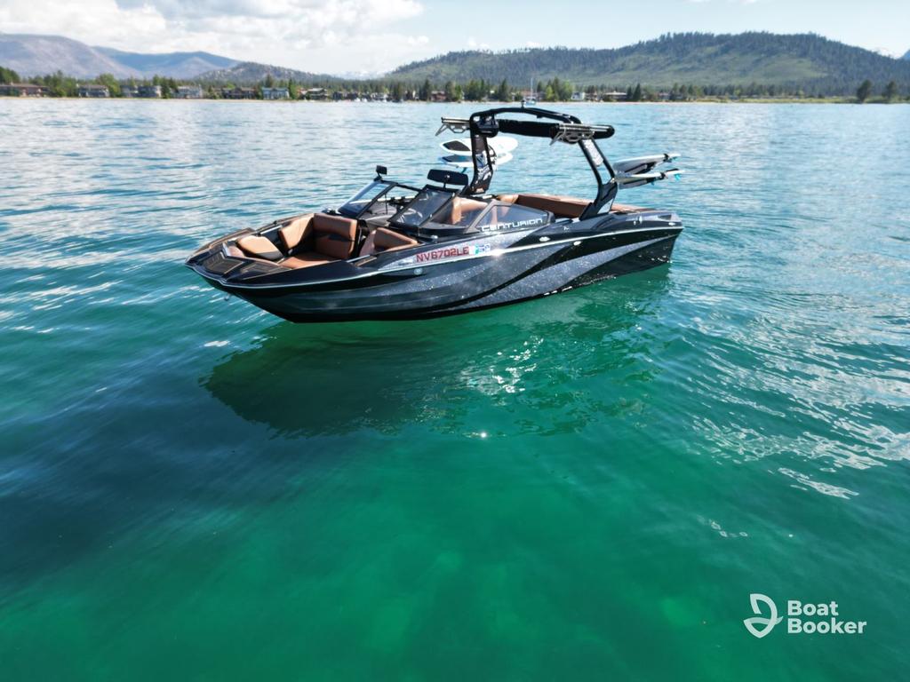 A black and brown motorboat's floating on clear turquoise water, with mountains and trees in the background.