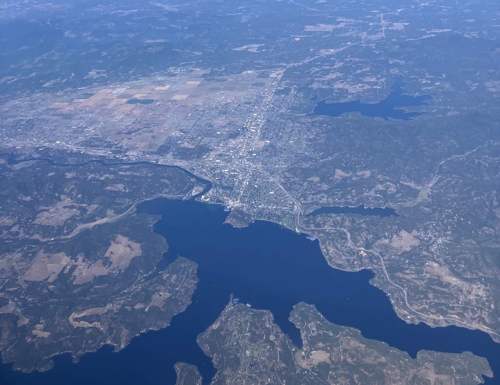 Here's an aerial view of a city that's bordered by lakes and rivers, where you can see urban, rural, and forested areas all under clear skies.