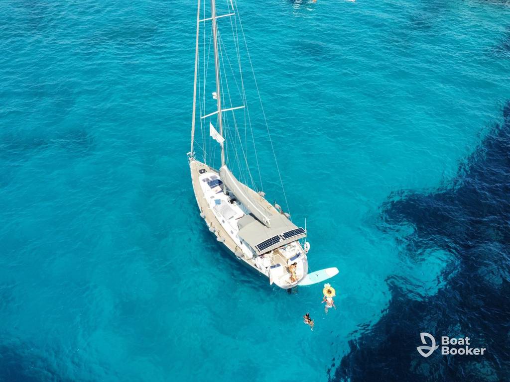 A sailboat's anchored in clear blue water with people swimming nearby; the Boat Booker logo's visible in the corner.