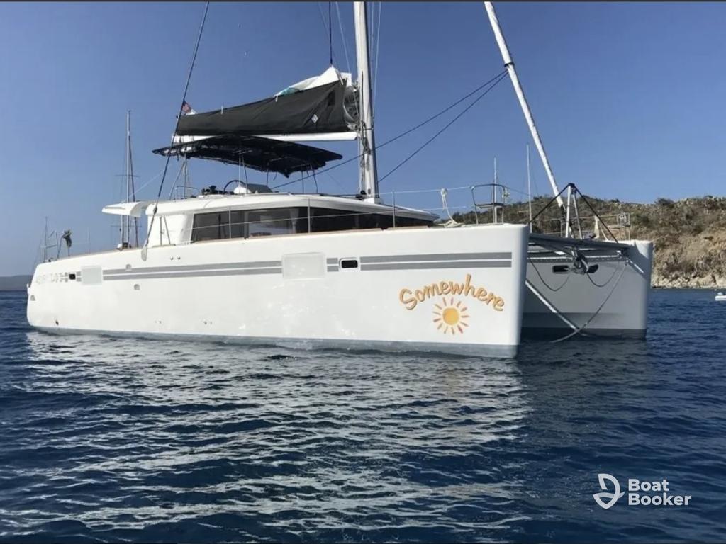 A white catamaran called "Somewhere" is anchored in calm Blue water near a rocky coast. It's sunny with clear skies, and there aren't any FISH or other SPECIES visible in the scene.