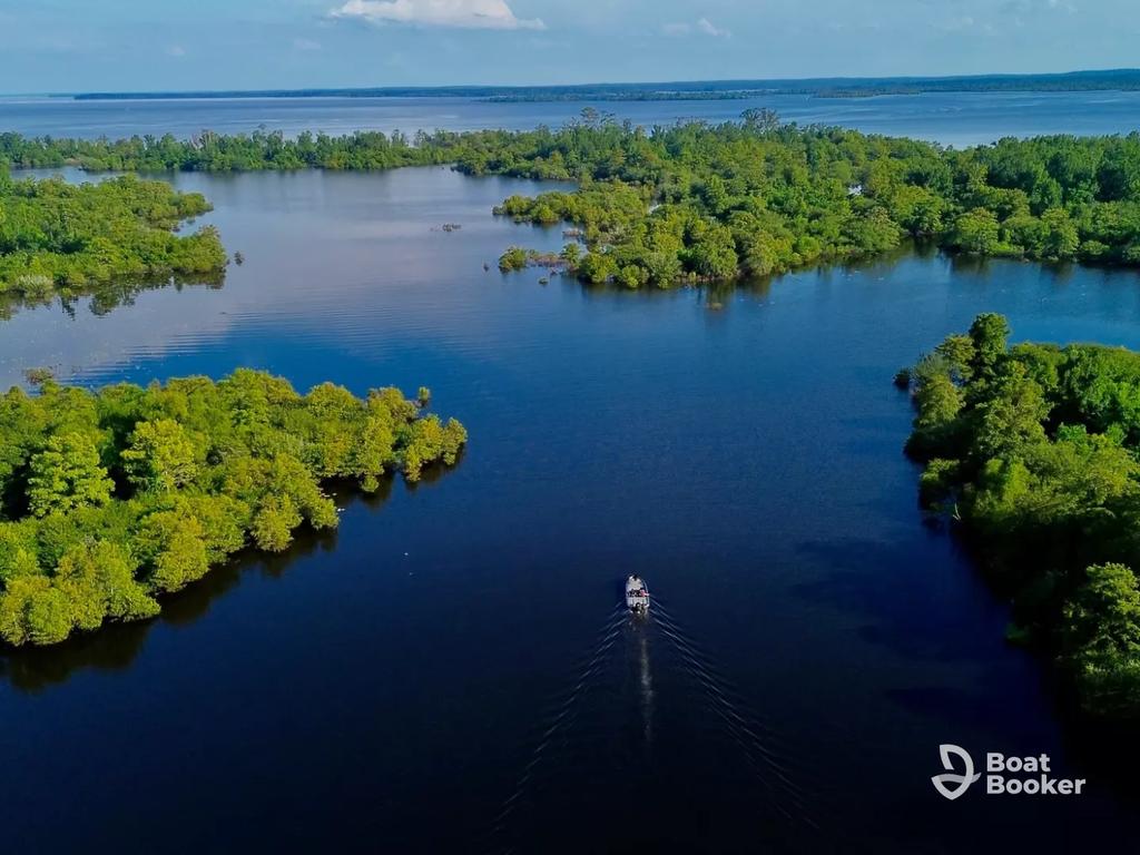 You’re looking down at a small boat gliding across a calm, tree-lined lake with islands under a blue sky. The "Boat Booker" logo’s in the corner. No fish or species are visible here.
