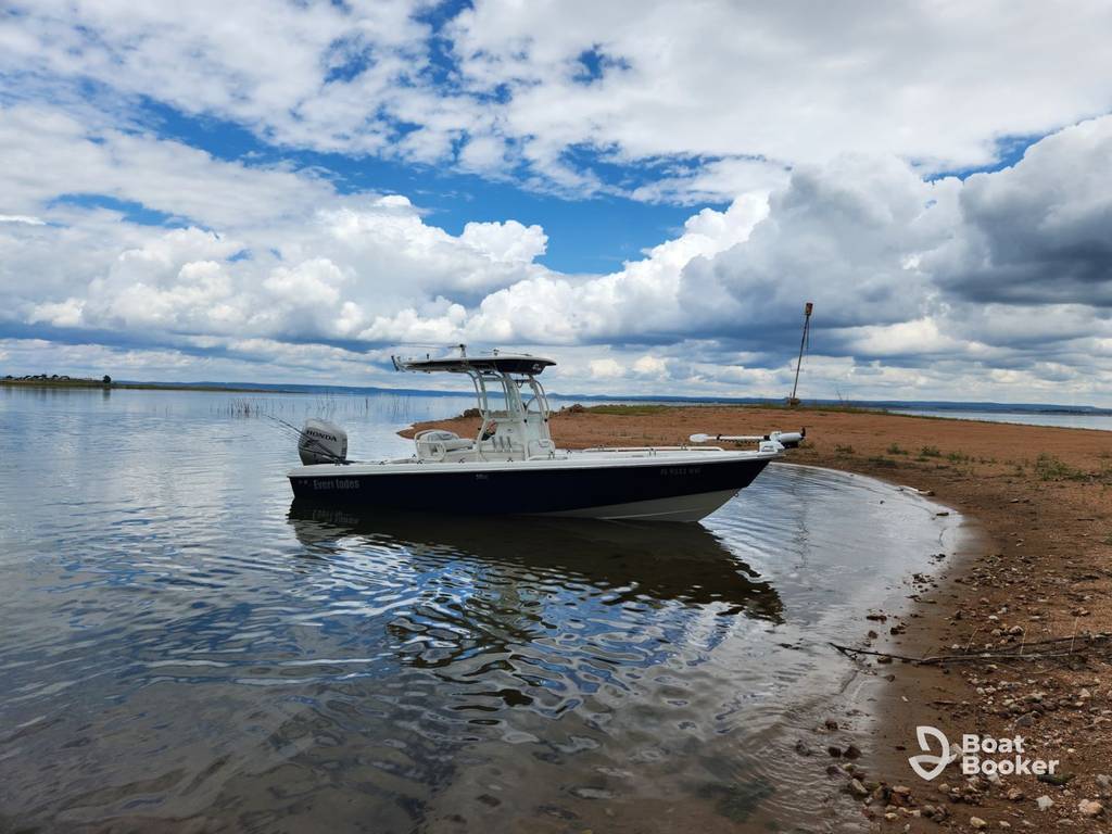 There's a small motorboat anchored near the shoreline of a calm lake under a mostly cloudy sky, with sand and water in the foreground.