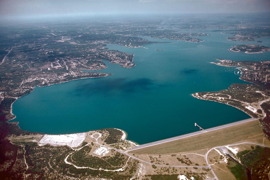 You’re looking at an aerial view of a big lake surrounded by land, with a dam at the bottom right and scattered buildings and roads dotting the landscape.