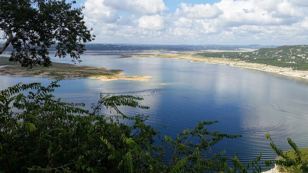 You’re looking at a big lake bordered by greenery, with a partly cloudy sky overhead and gentle ripples on the water’s surface.