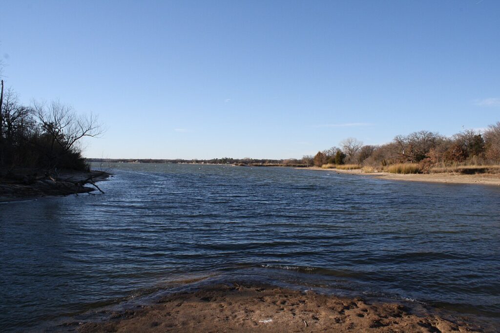 A calm river with a rocky shoreline and leafless trees on both sides under a clear blue sky.