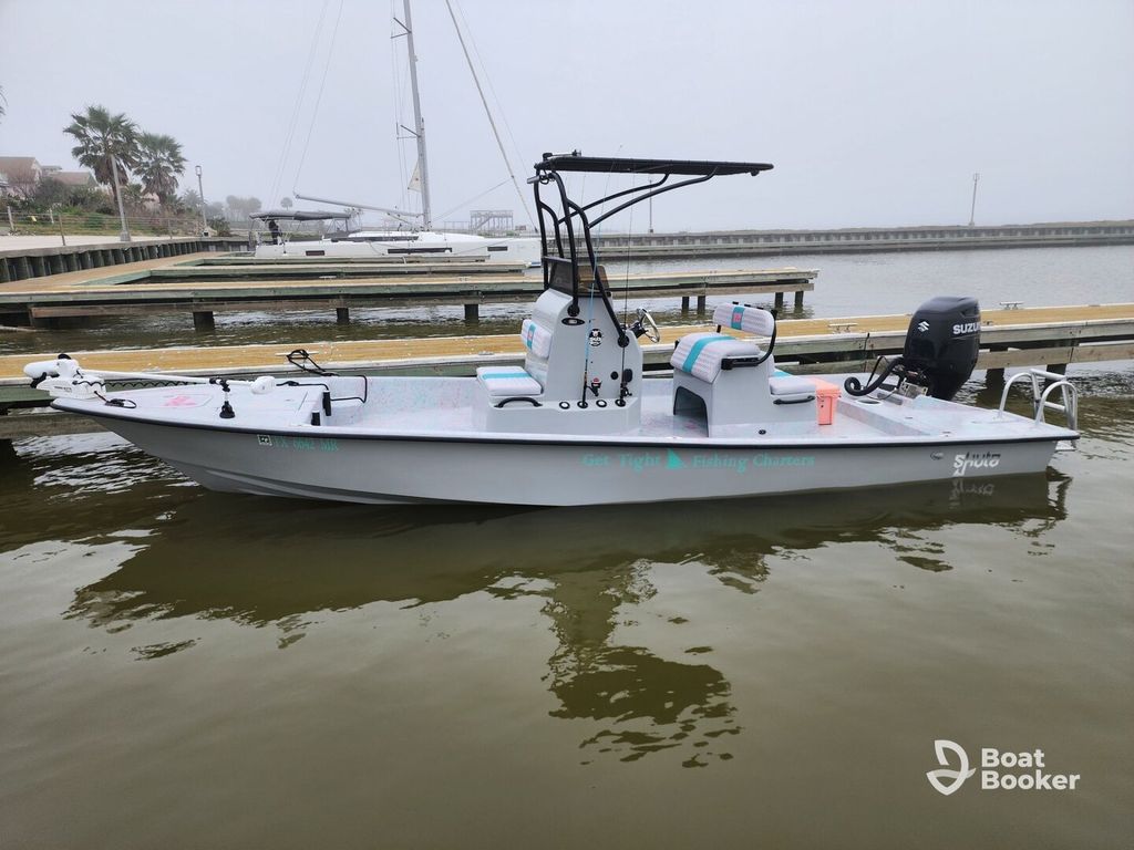 A gray fishing boat with a center console and striped seating's docked in a marina with calm water and one sailboat in the background.