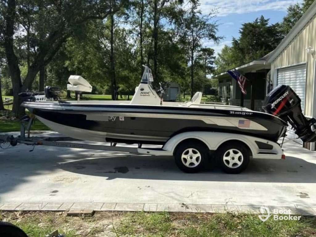 Black and white Bass fishing boat with outboard motor on a dual-axle trailer, parked on a concrete driveway next to trees and a lawn.