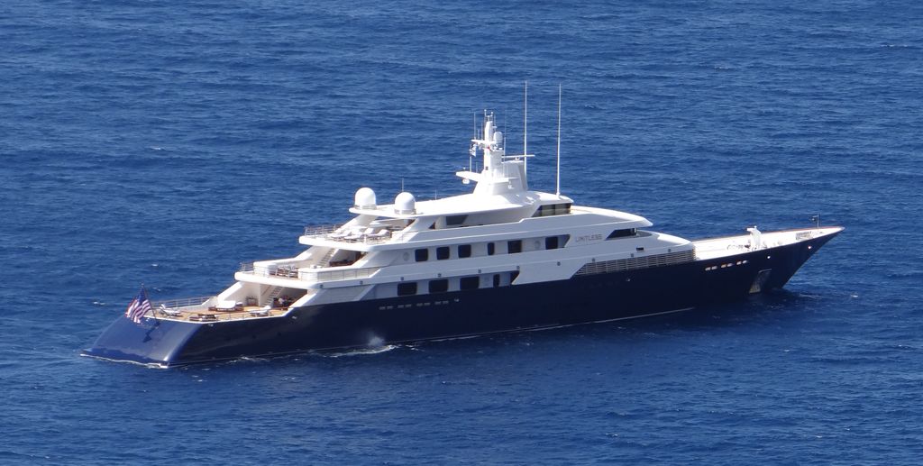 A large luxury yacht with a dark hull and white superstructure's sailing on calm blue water.