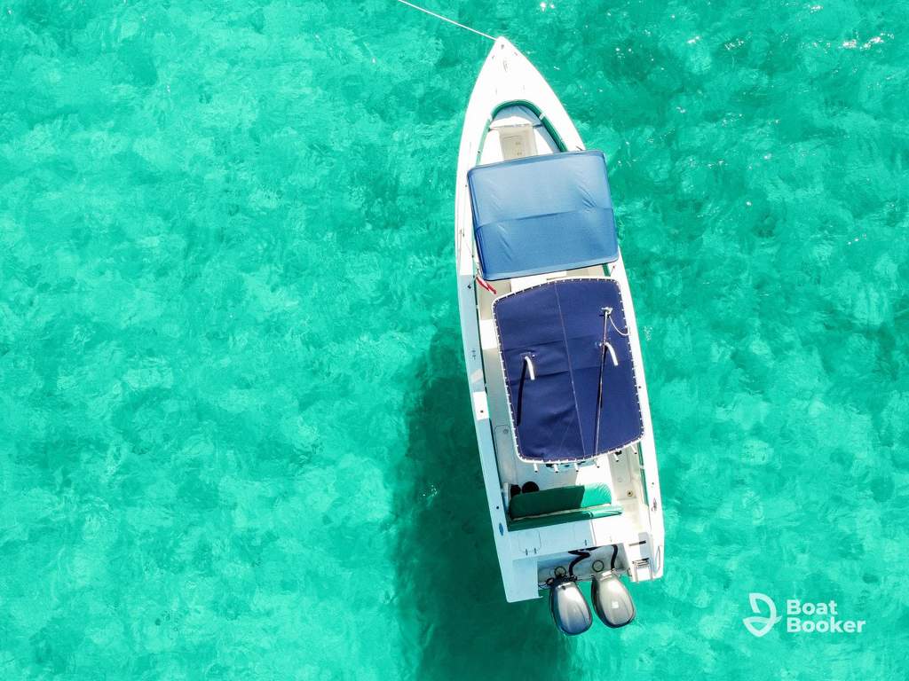 You're looking down at a white motorboat with blue canopies floating on clear turquoise water, and there's "Boat Booker" branding in the corner.