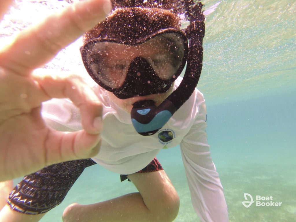 Someone's underwater in a snorkel mask and swim shirt, giving an "OK" hand sign. The BoatBooker logo shows in the bottom right corner.