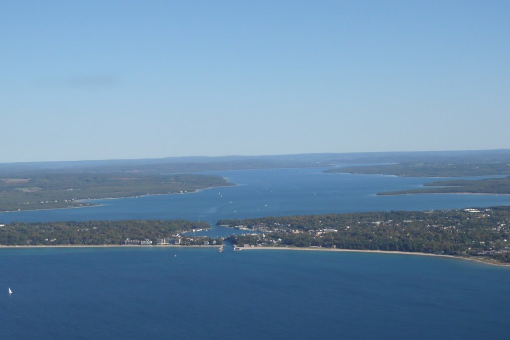 You’re looking at a big lake edged by green land and a sandy shoreline, with small boats on the water below a clear blue sky.