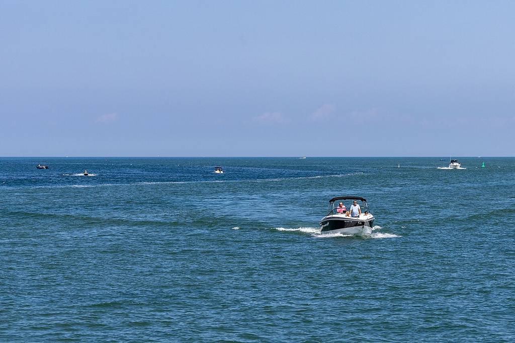 A motorboat with people aboard's cruising on open blue water, with several other boats in the distance under a clear sky.