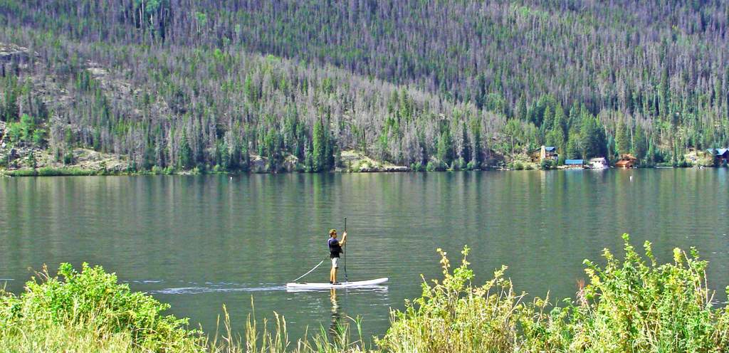Paddle boarder on calm Grand Lake with mountain backdrop in Colorado