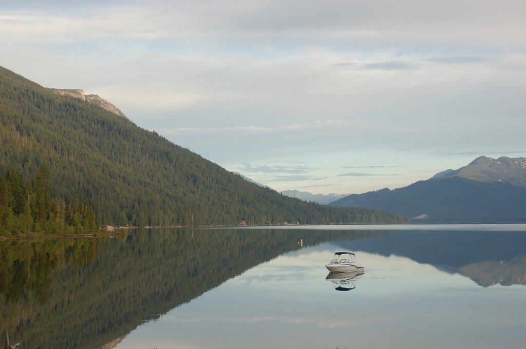 A small motorboat's floating on a calm lake—one of the best in Washington State—surrounded by forested mountains, their reflections shimmering on the water.