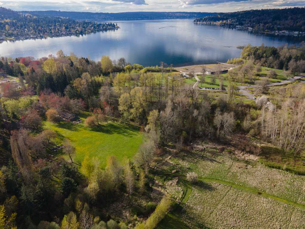 You’re looking at an aerial view of a lakeside park—one of the best boating lakes in Washington State—with grassy fields, scattered trees, and calm water below a partly cloudy sky.