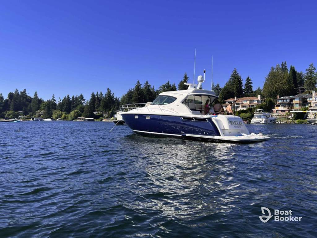A white and blue motor yacht's anchored on one of Washington state’s top boating lakes, near houses and trees along the shore under a clear blue sky.