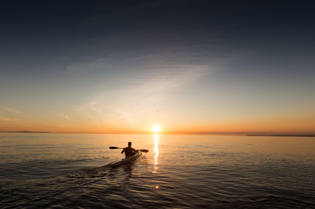 Silhouette of a kayaker paddling at sunset on calm water