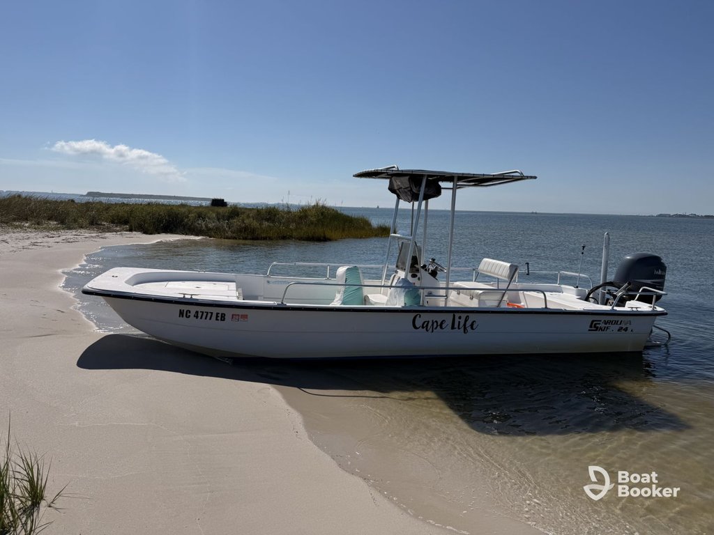 A white motorboat called "Cape life" is beached on a sandy shore next to calm water under a clear sky.