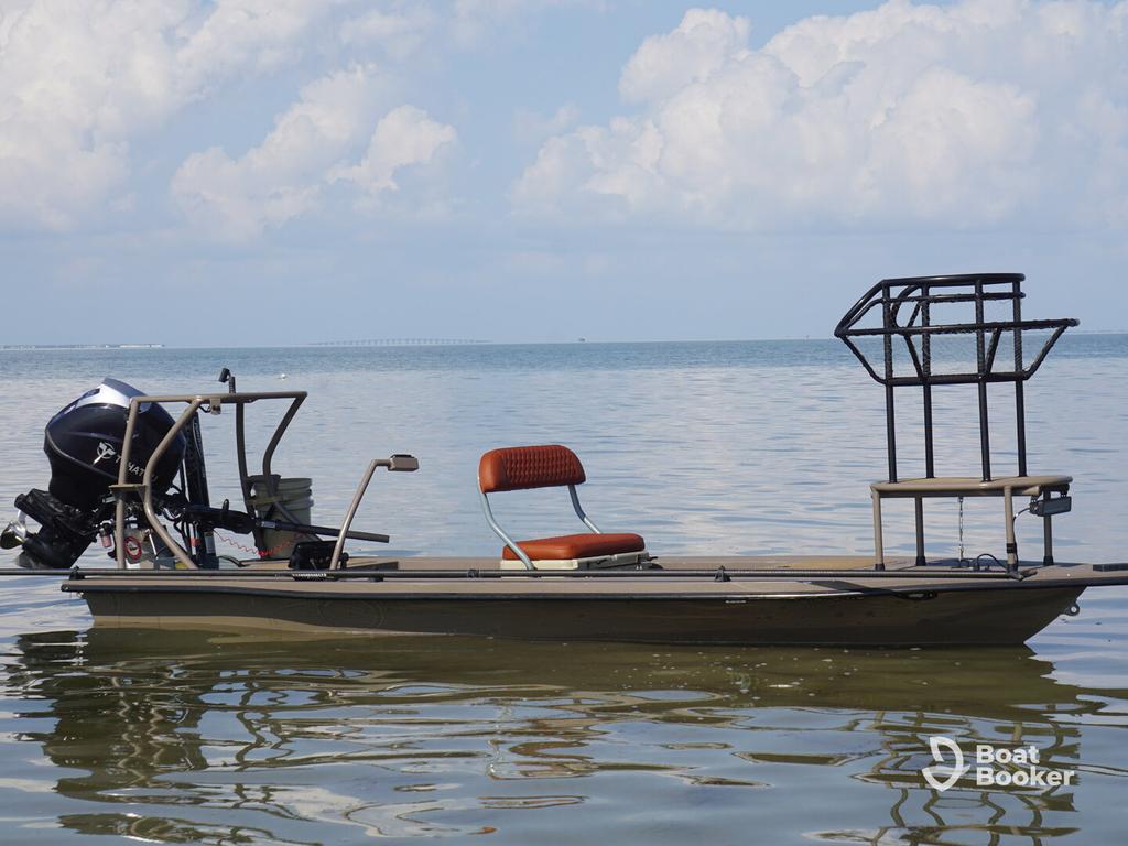 A small flat-bottom boat with an outboard motor and one orange seat floats on calm water—it’s a classic skiff boat—beneath a cloudy sky.