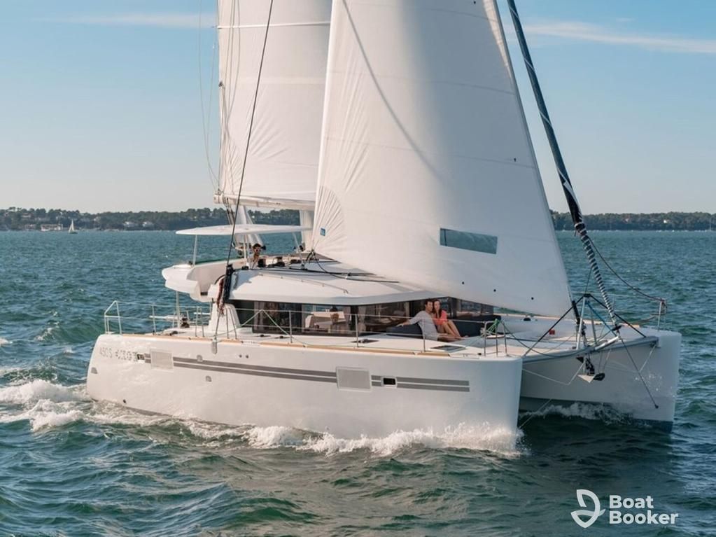 A white catamaran sailboat, perfect for sailing one-oh-one, glides over the water with two people onboard. The “Boat Booker” logo’s in the lower right corner.