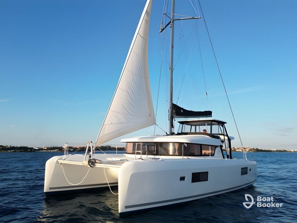 A white catamaran yacht’s sailing on calm blue water—a perfect scene for a Sailing 101 adventure near the distant coastline under a clear sky.