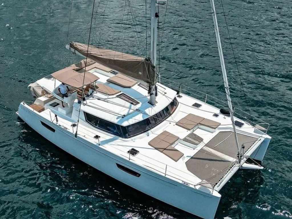 A white catamaran yacht with tan canopies and cushions sails on calm blue water; two people at the helm are enjoying their own Sailing 101 adventure.