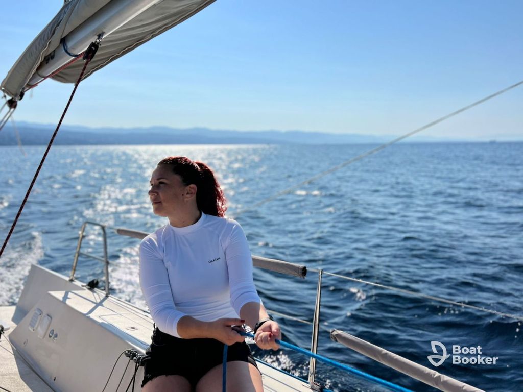 Someone’s in a white long-sleeve shirt, sitting on a sailboat holding a rope—classic sailing one-oh-one—calm blue sea and far-off land under a clear sky. Boat Booker logo’s in the corner.