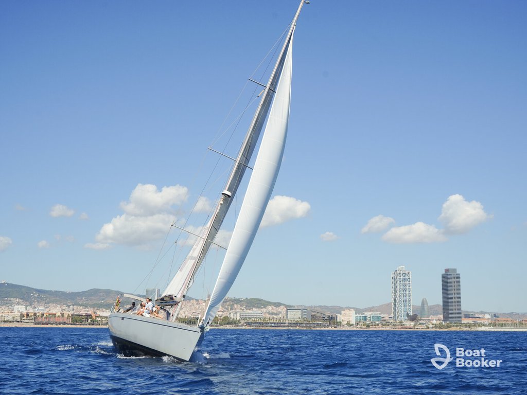 A sailboat’s leaning to one side, showing sailing 101, as it glides through the water with a city skyline and modern buildings behind. No fish or species are shown.