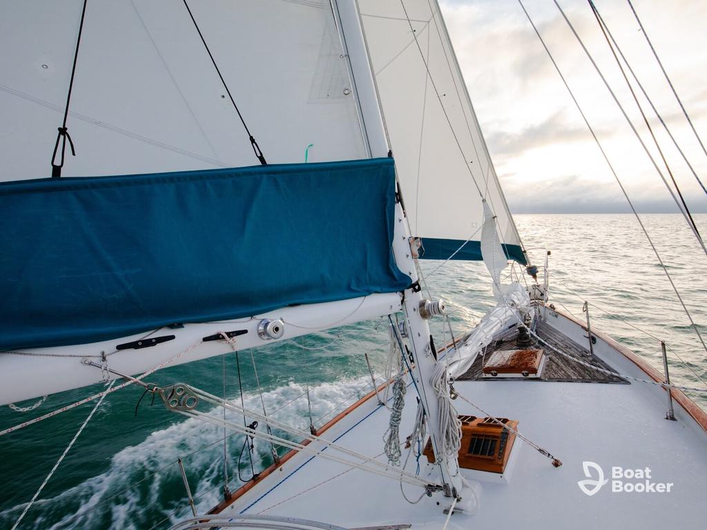 Experience sailing one-oh-one from the deck as your boat glides through calm waters, white sails raised against the low sun on the horizon.