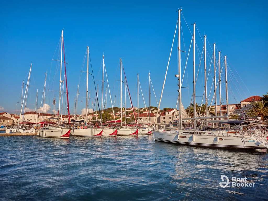 Several sailboats are docked in a marina, giving off a Croatian sailing vibe. You’ll see palm trees, calm waters, and a clear blue sky—that all makes for a picturesque scene.