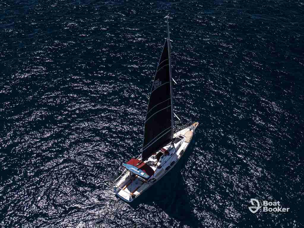 A single sailboat with a dark sail’s gliding through deep blue water, sunlight shimmering—a stunning glimpse of sailing in Croatia. The Boat Booker logo’s in the bottom right corner.