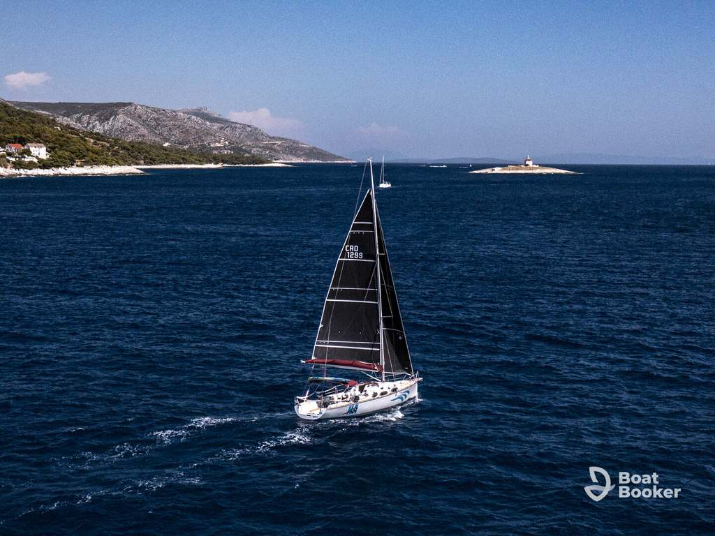 A sailboat with black sails glides across deep blue water, sailing in Croatia past a small island and lighthouse under a clear sky.